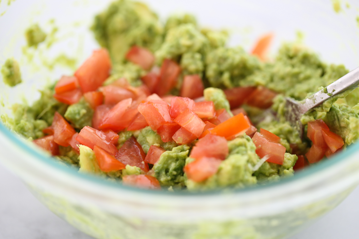 guacamole in a white bowl surrounded by chips