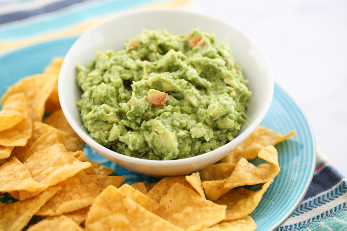 guacamole in a white bowl surrounded by chips