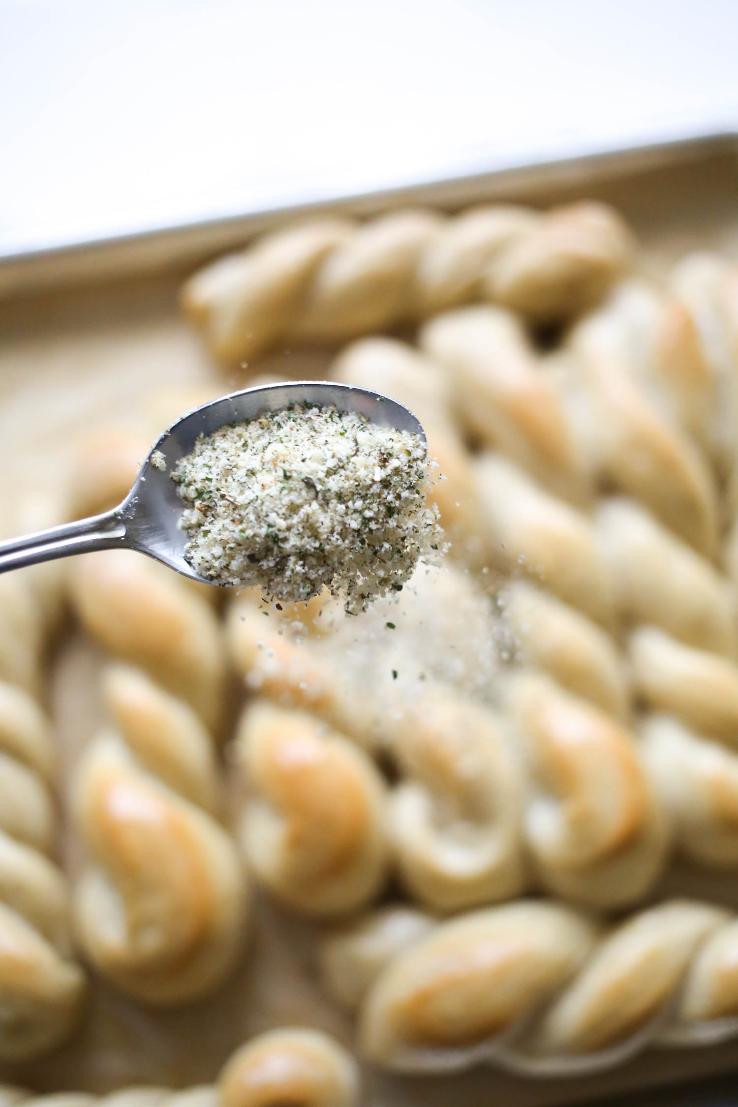 sprinkling garlic bread seasoning on breadsticks from Our Best Bites