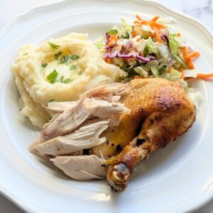A plate of rotisserie-style "fauxtisserie" chicken served alongside mashed potatoes and salad.