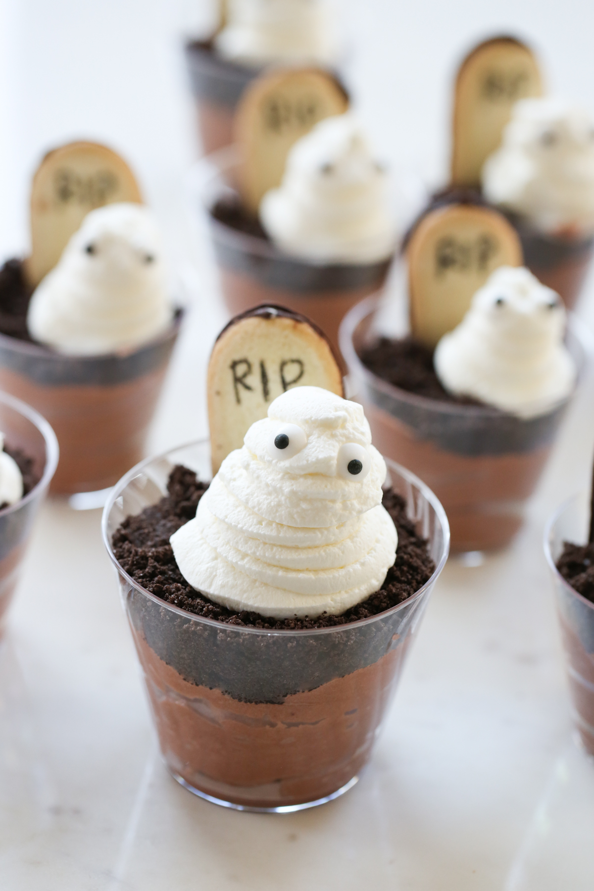 A dessert cup filled with pudding, a cookie headstone, and a whipped cream ghost.