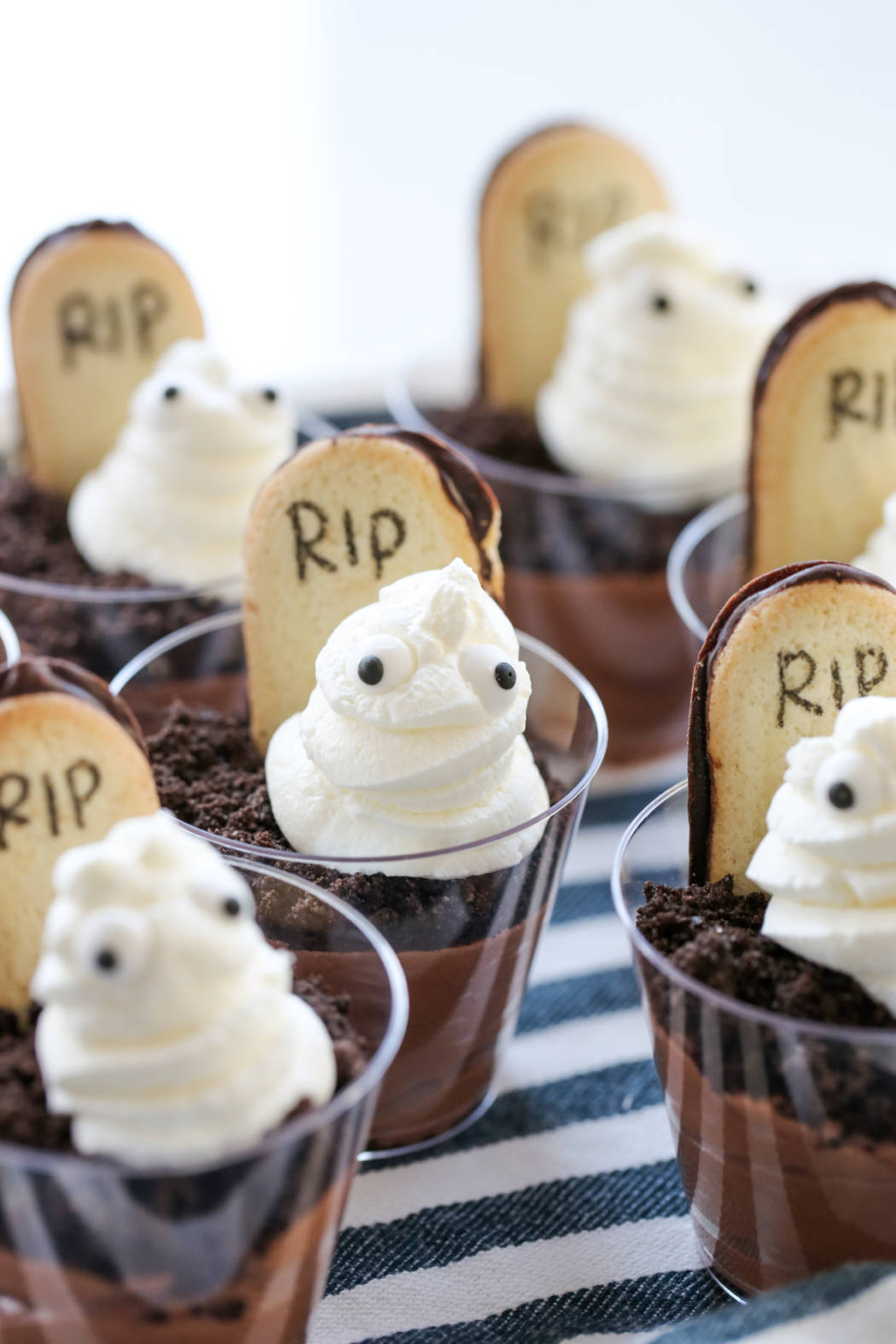 A dessert cup filled with pudding, a cookie headstone, and a whipped cream ghost.