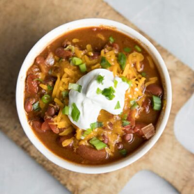 A bowl of chili topped with sour cream, cheese, and green onions.