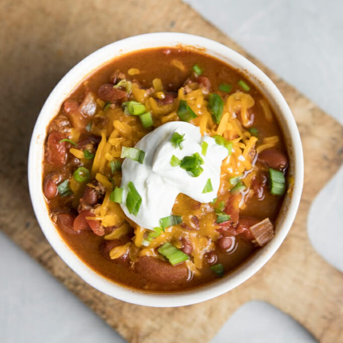 A bowl of chili topped with sour cream, cheese, and green onions.