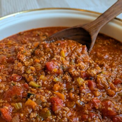 A pan of rich pasta sauce full of veggies and Italian sausage with a wooded spoon.