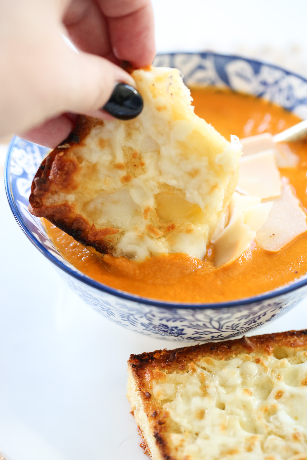 toasted bread being dipped in tomato soup