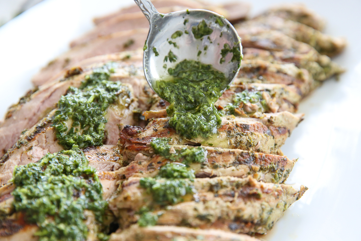 spooning chimichurri over pork tenderloin