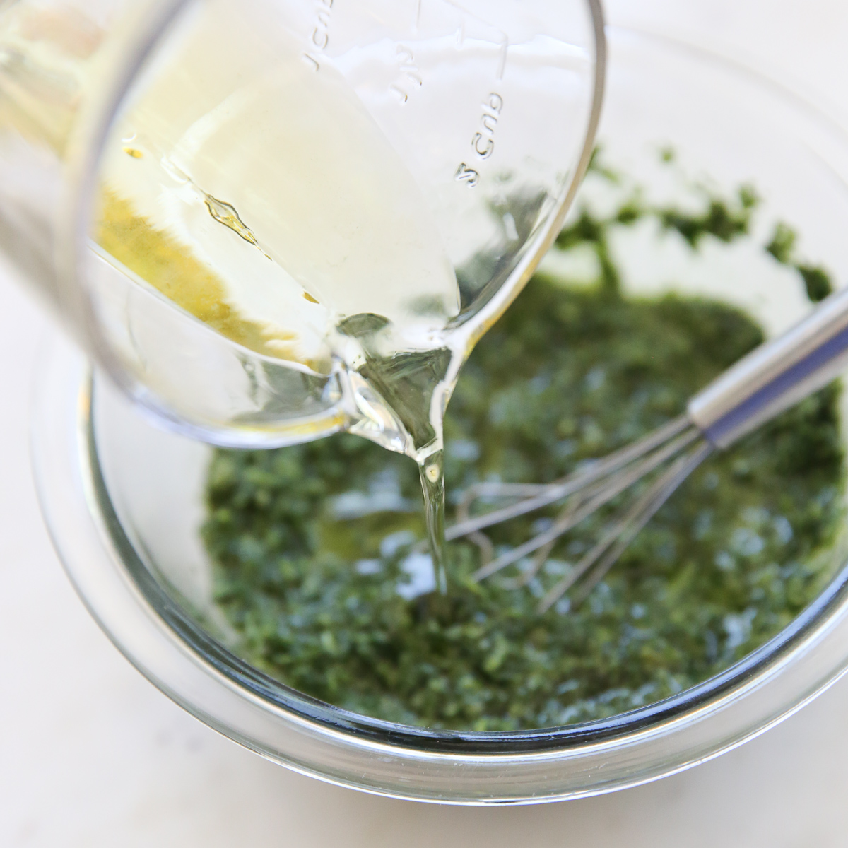 pouring oil into a bowl of chimichurri sauce