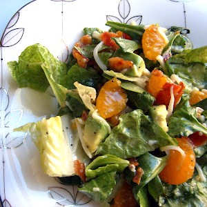 A close up of a delicious salad full of greens, mandarin oranges, avocados, bacon, and cheese, tossed in a sweet poppyseed dressing.