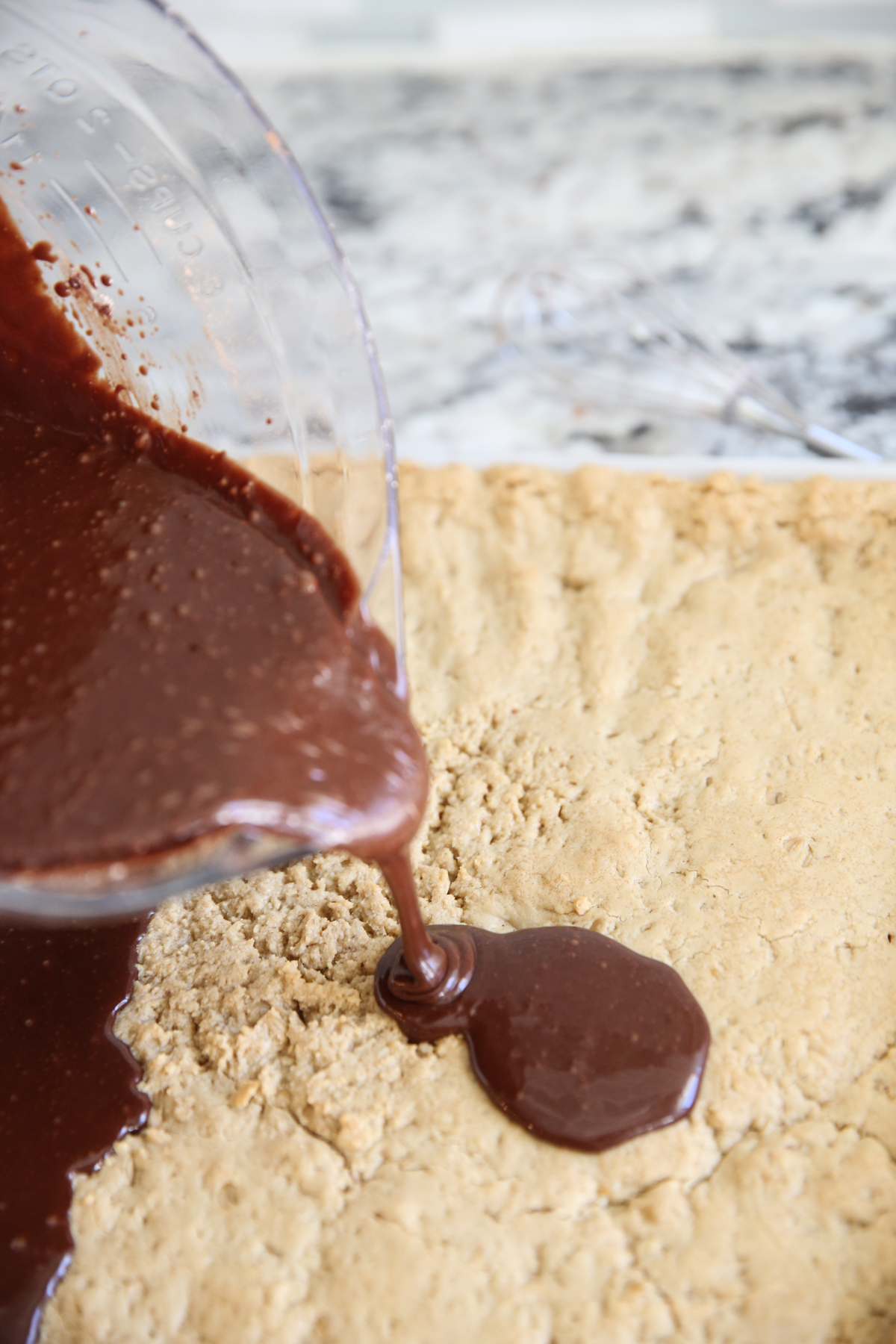 pouring chocolate icing on cookie bars