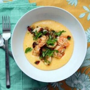 A bowl of grits, topped with shrimp and bacon.