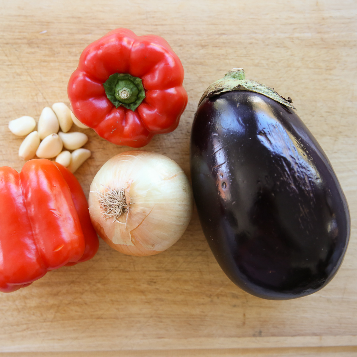 eggplant, peppers, onion, and garlic on a cutting board