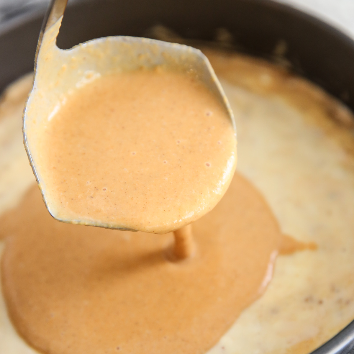 pouring pumpkin pie batter on top of cheesecake