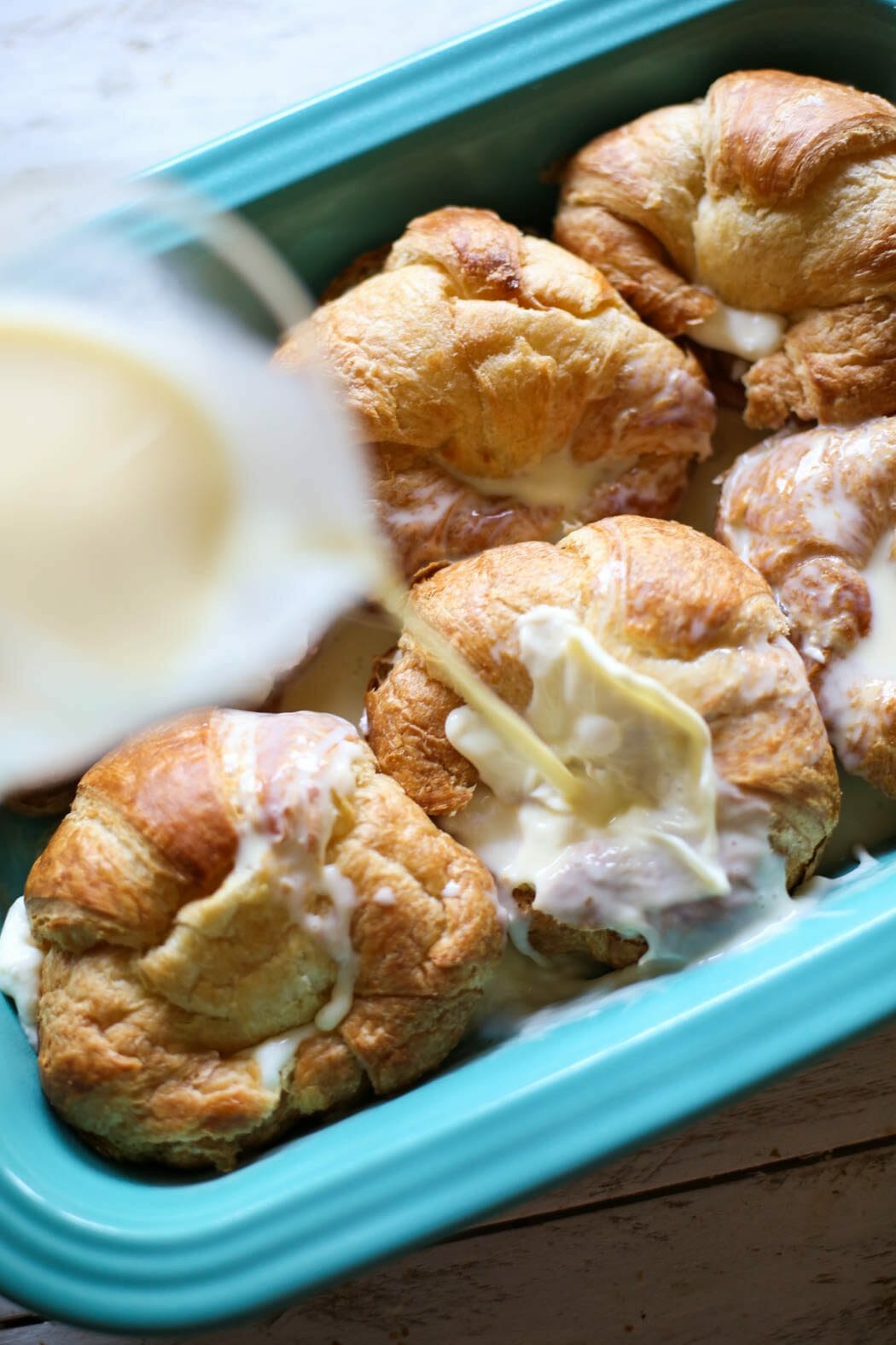 pouring french toast mixture over stuffed croissants