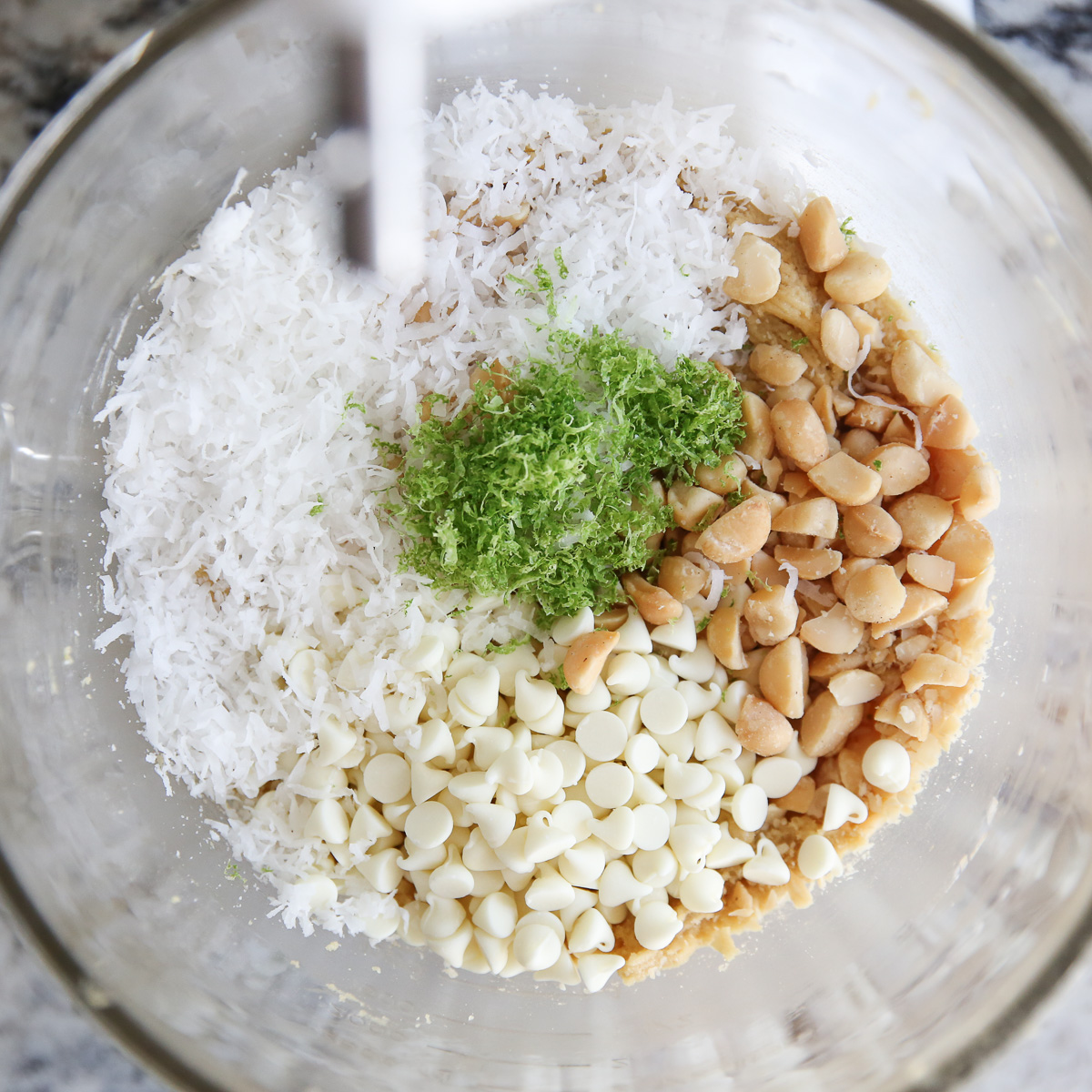 coconut, white chocolate chips, macadamia nuts, and lime zest getting mixed into cookie dough