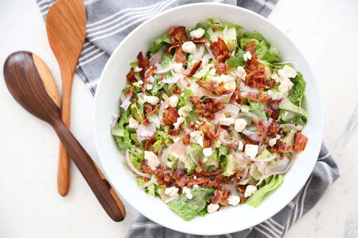 green salad in a white bowl with serving utinsels