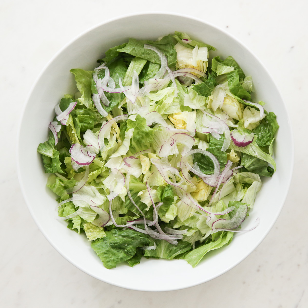 white bowl of lettuce with red onion