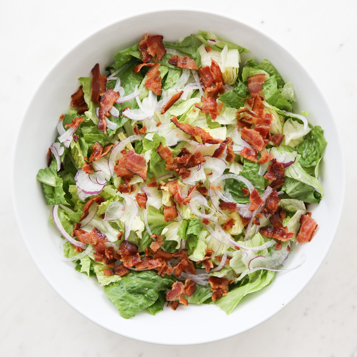white bowl of lettuce with bacon and onion
