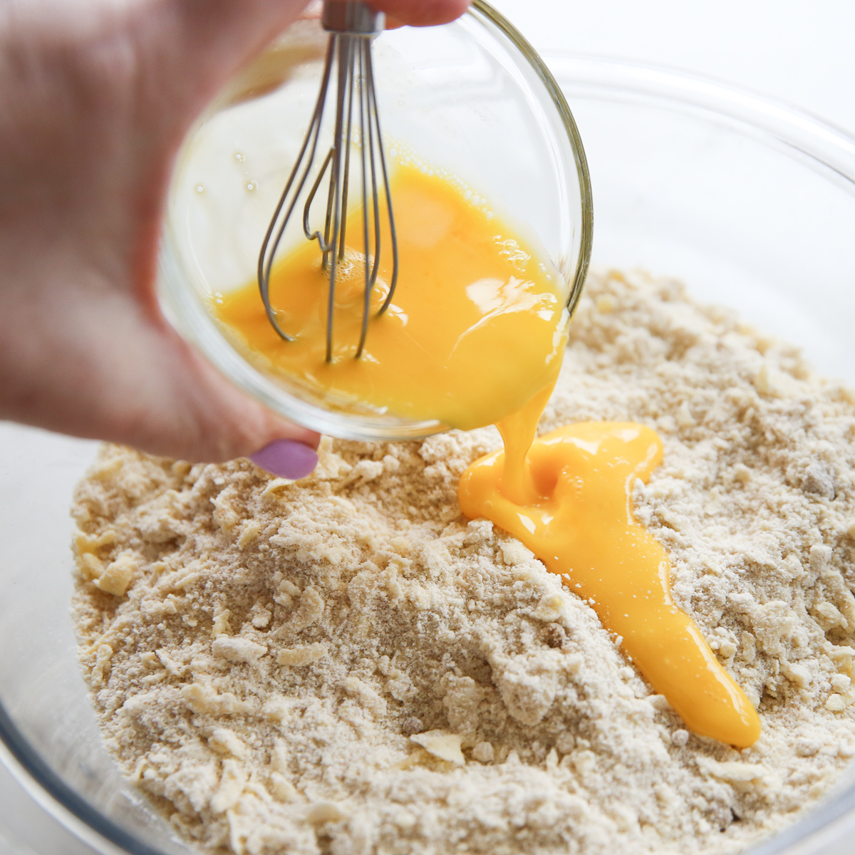whisked egg pouring into a bowl of dry ingredients
