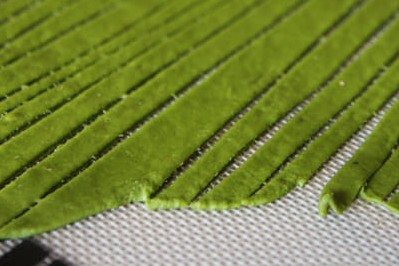 Green pasta dough made of spinach and basil, rolled and cut into noodles on a silpat mat.