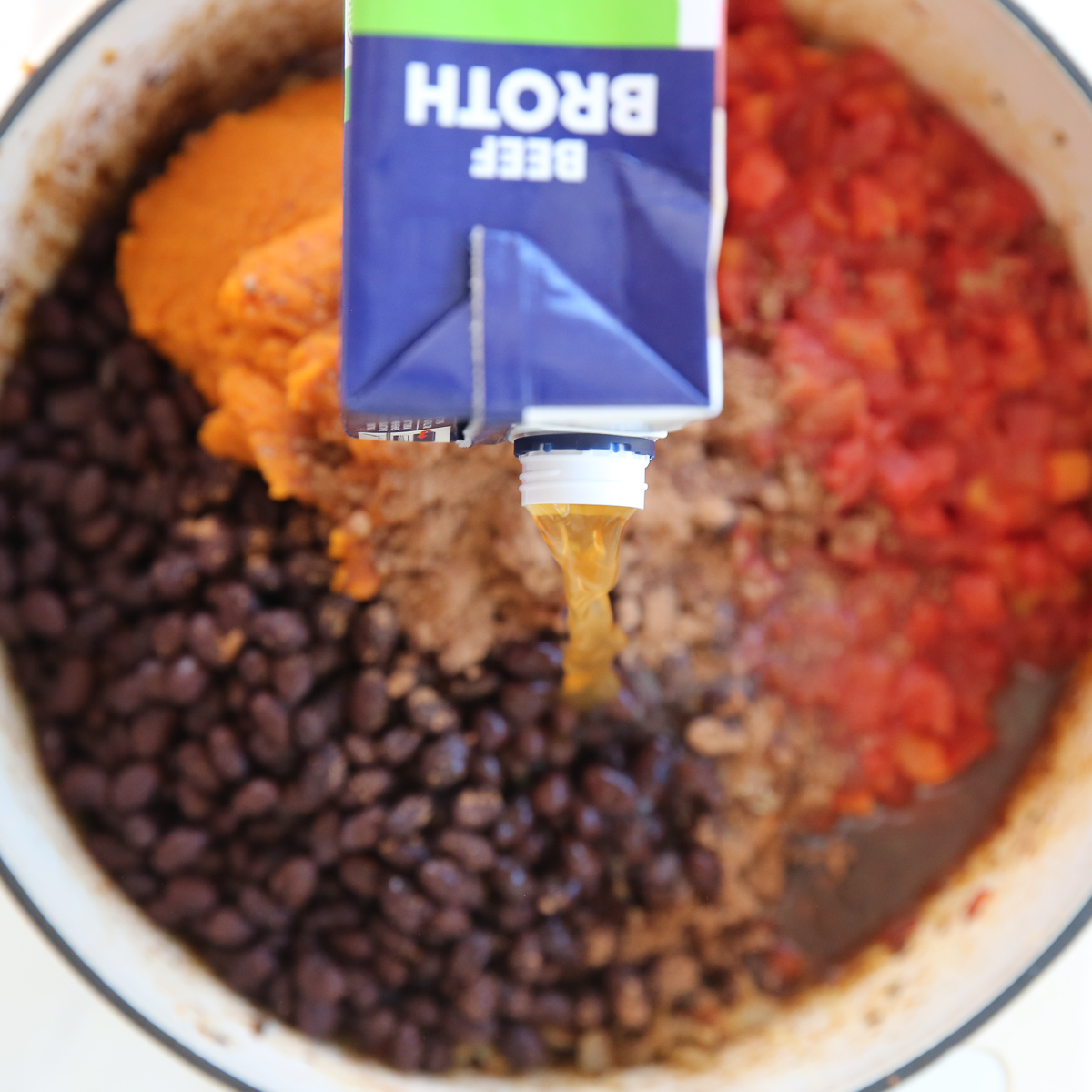 pouring beef broth into chili