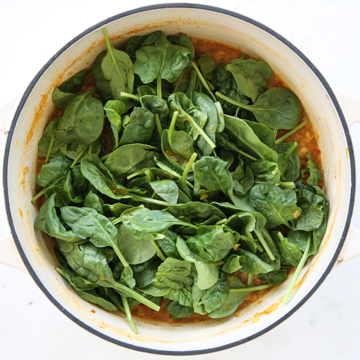 adding spinach to a pot of red lentils