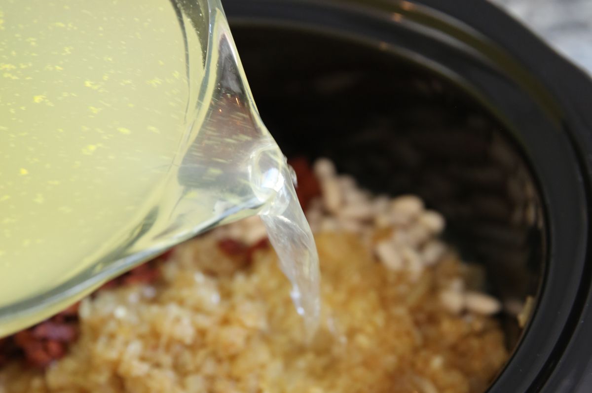 pouring broth into a slow cooker of beans