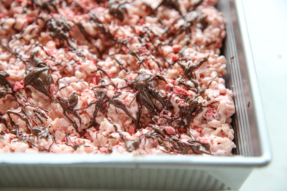 pink rice krispie treats in a pan drizzled with chocolate and berries