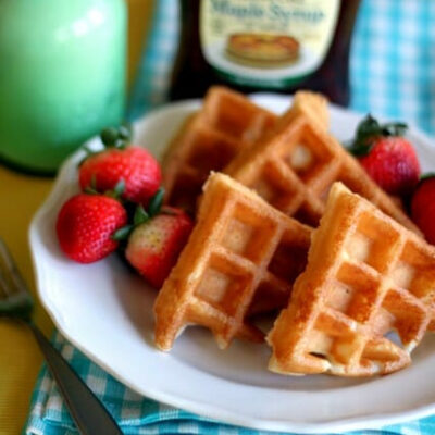A stack of Belgian waffle quarters on a white plate with whole strawberries.