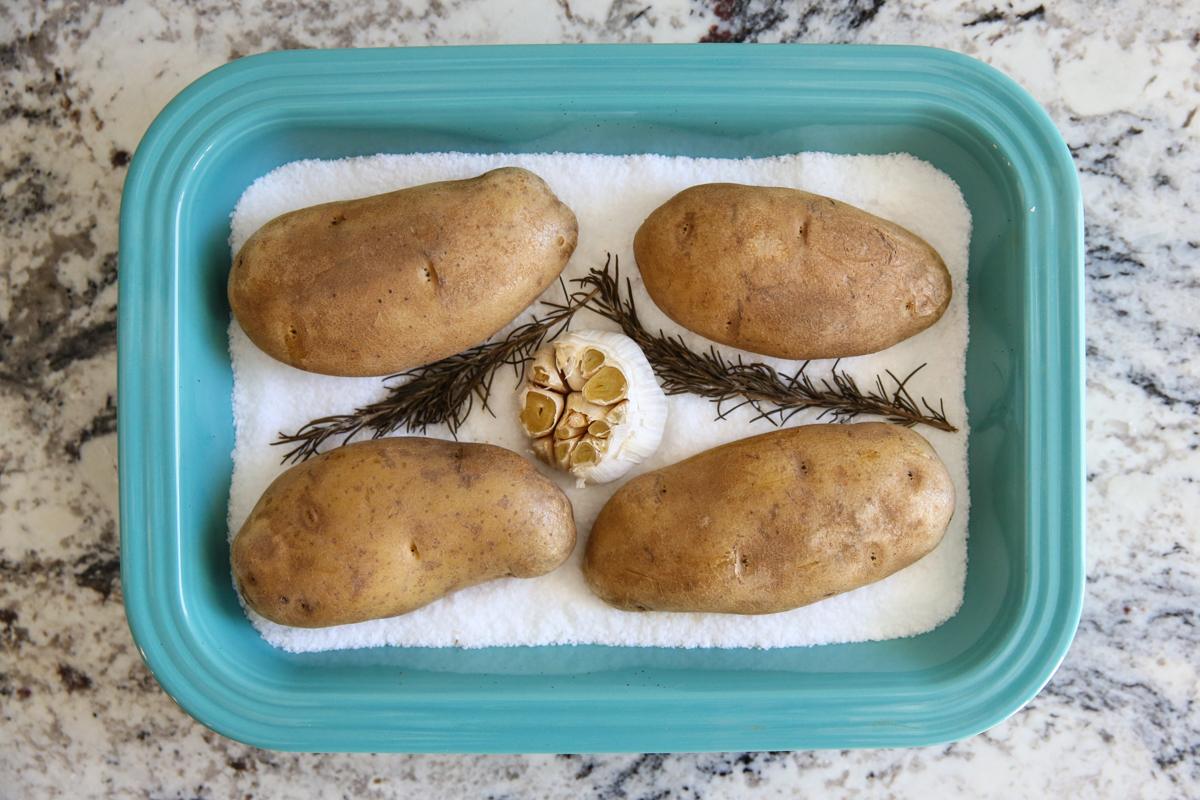 roasted garlic and rosemary with potatoes in a pan filled with salt