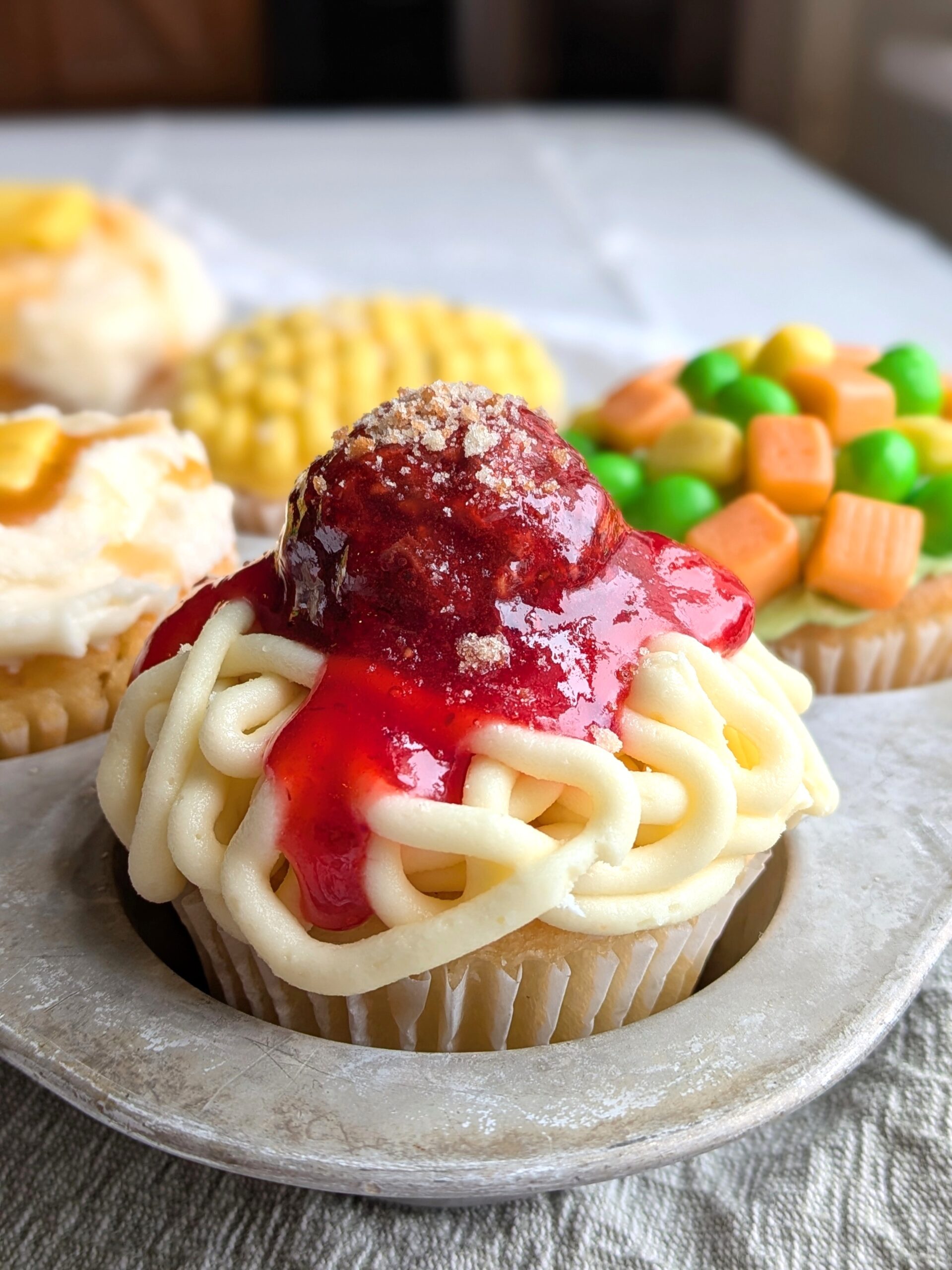 A funny cupcake with frosting squiggles and a candy meatball in strawberry sauce that looks like spaghetti and meatballs.