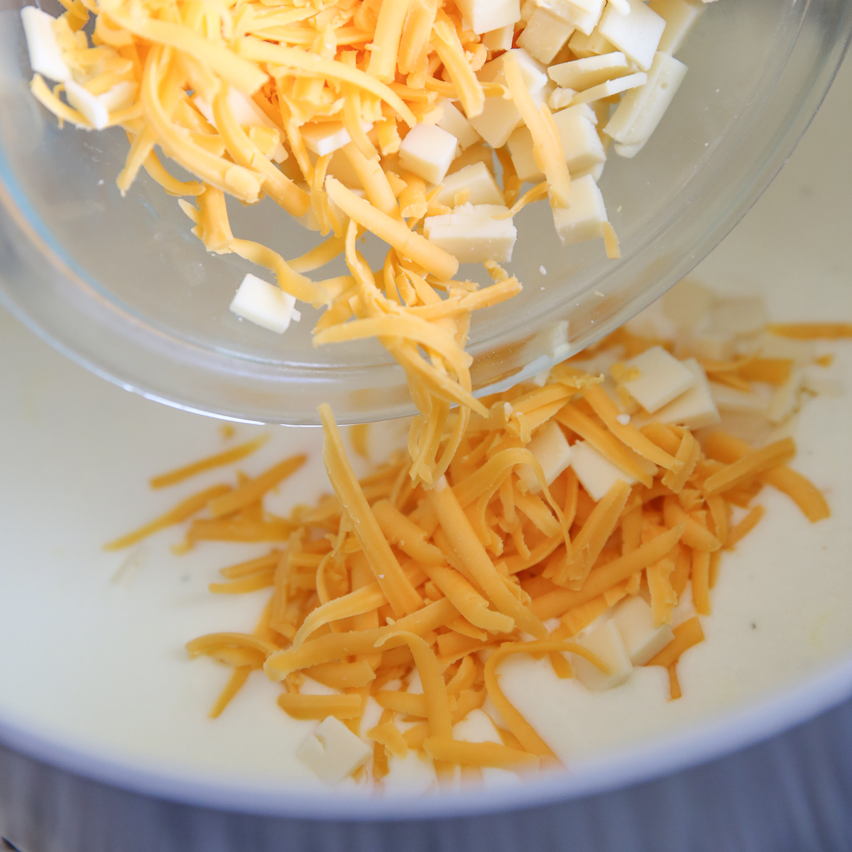 pouring cheese into a creamy sauce