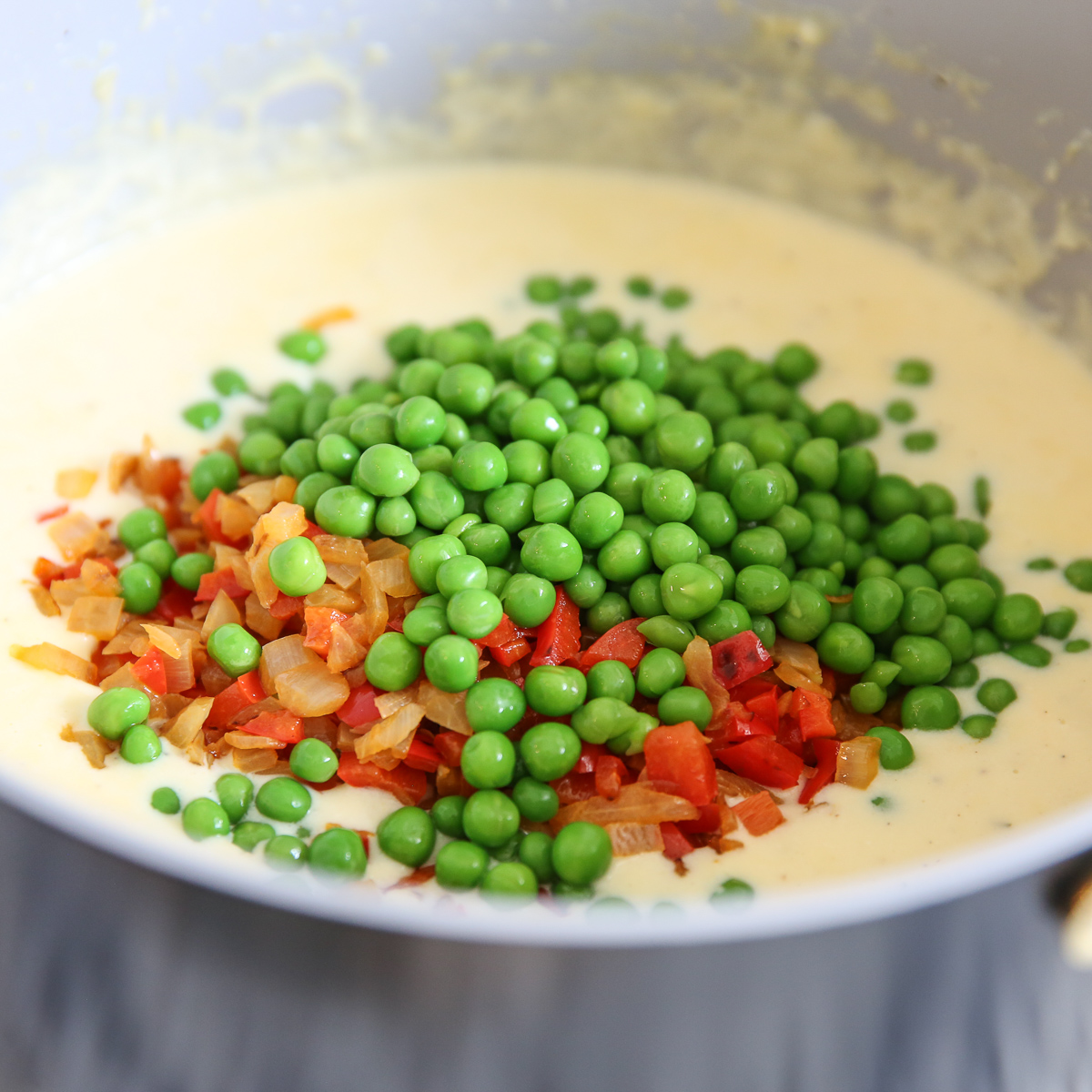 peas, peppers, and onions going into a cream sauce