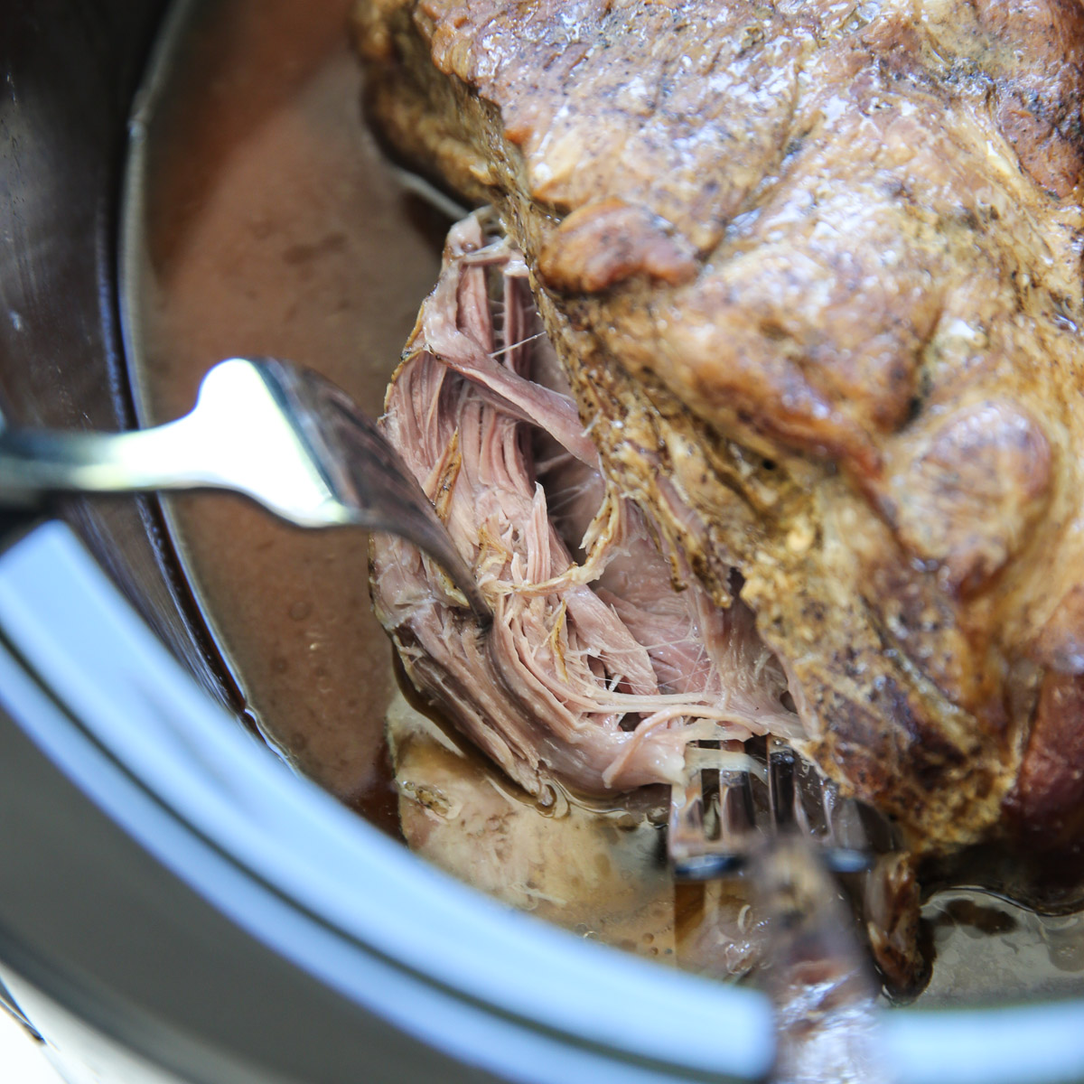 fork shredding a pork roast in a slow cooker