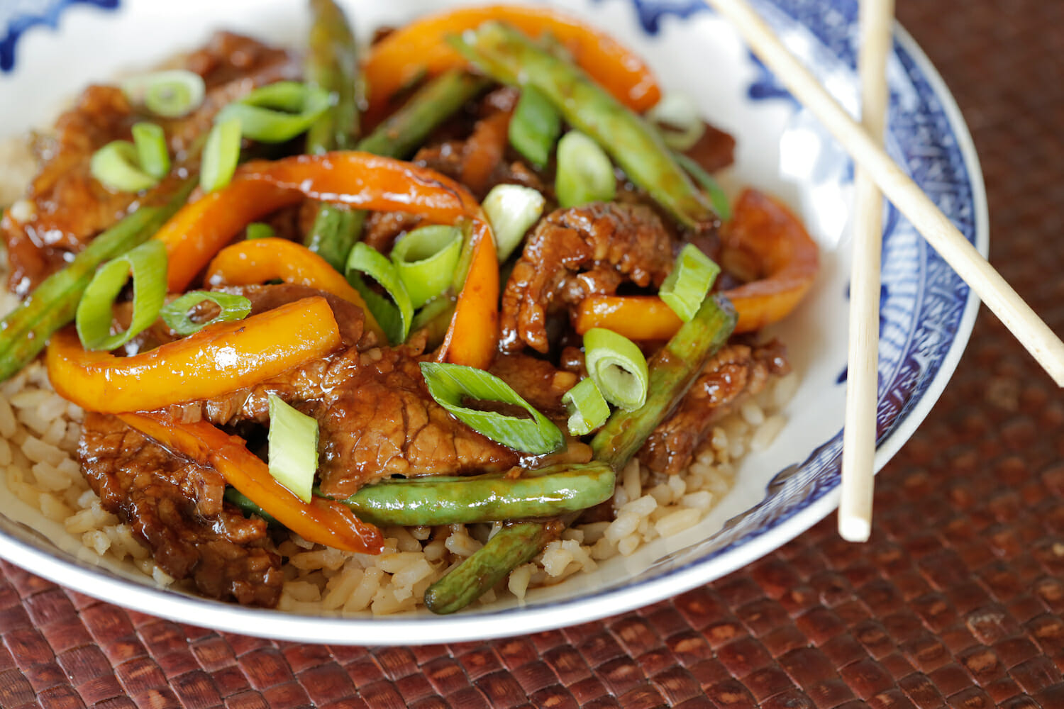 beef and green bean stir fry over rice in a blue bowl with chop sticks