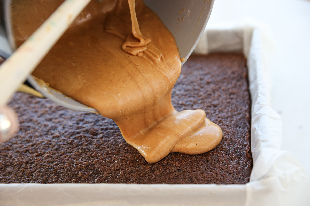 pouring peanut butter frosting over cake