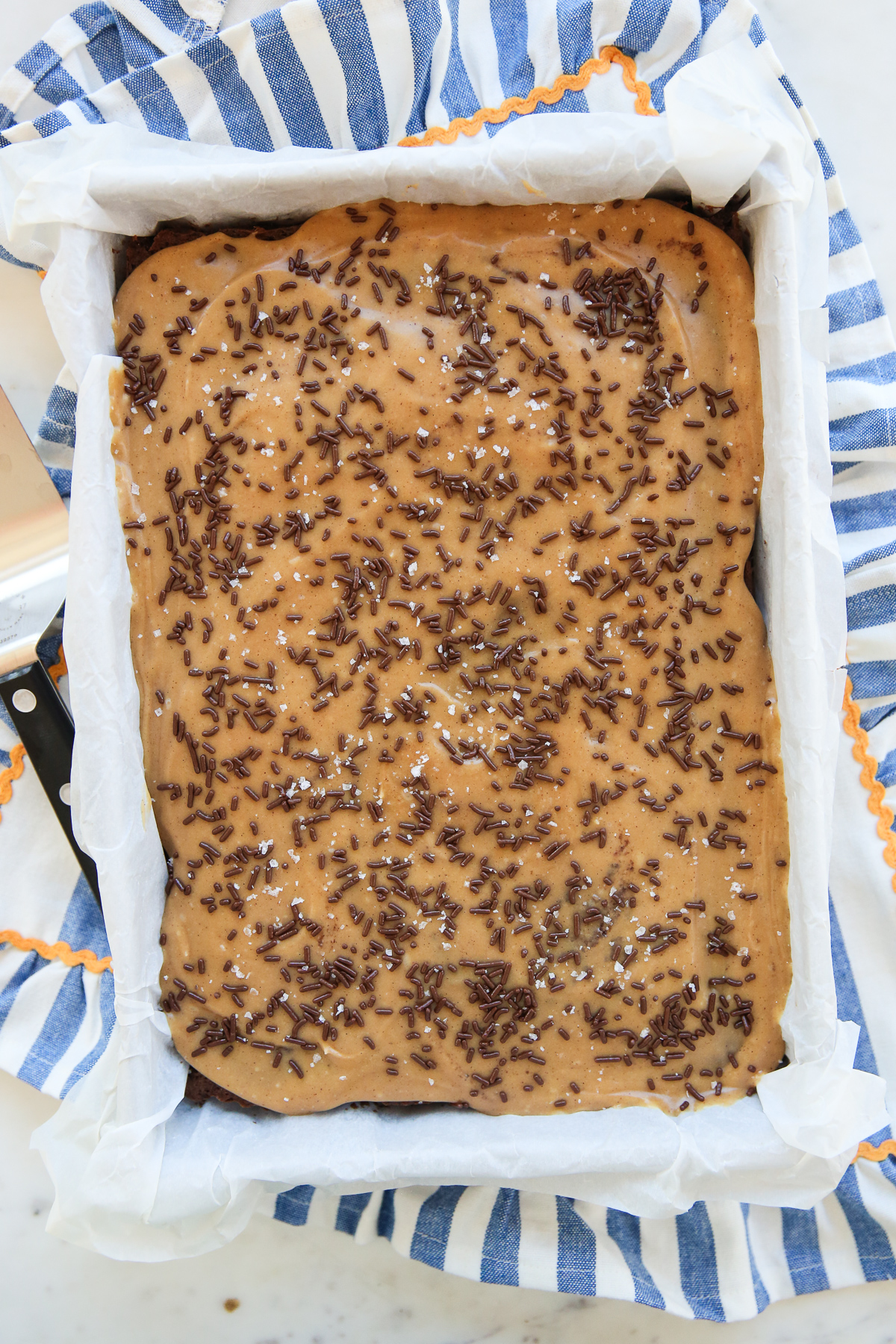 Chocolate Cake with peanut butter frosting in a cake pan with sprinkles and sea salt on top