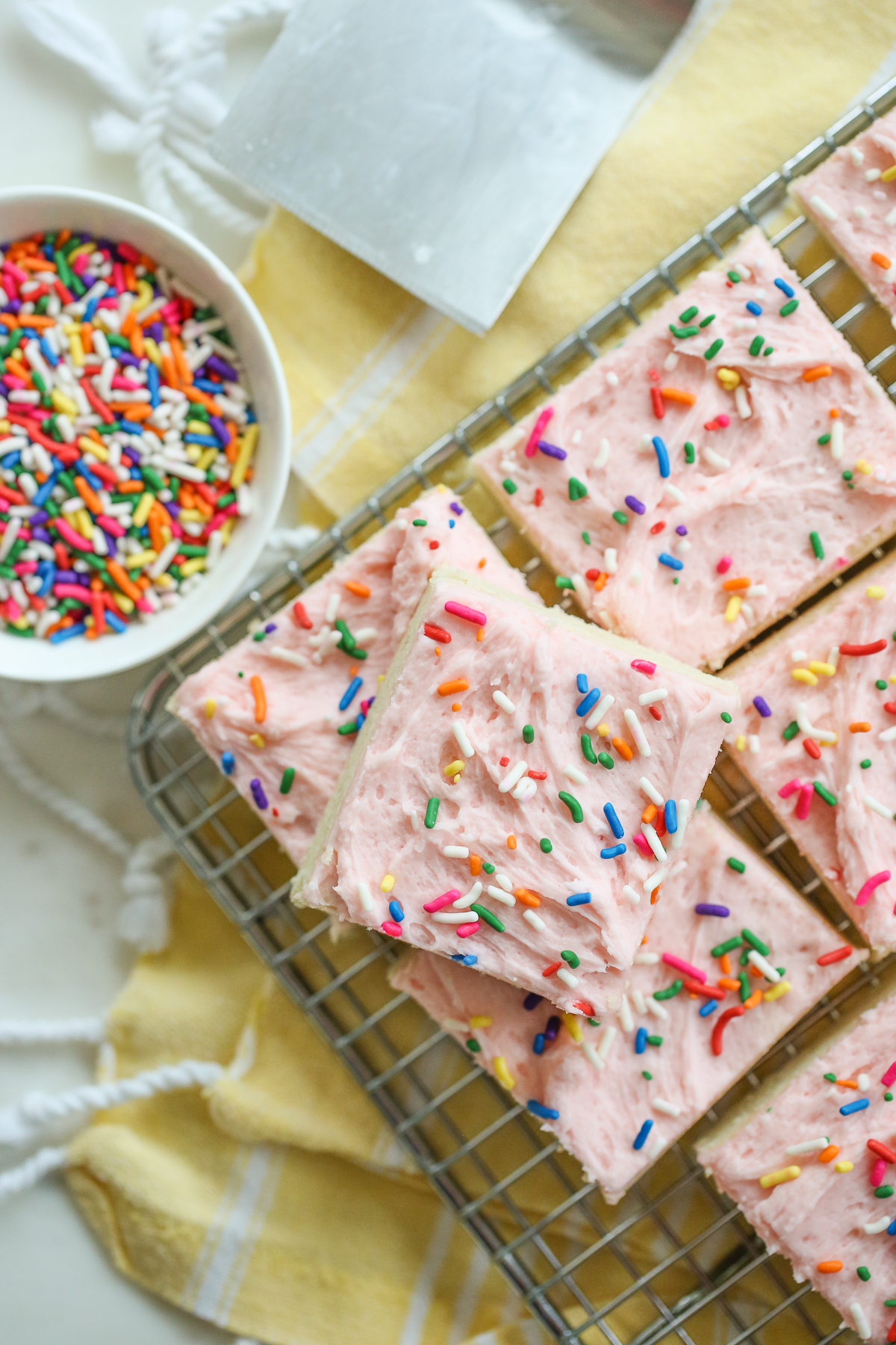 sugar cookie bars with pink frosting stacked on a tray