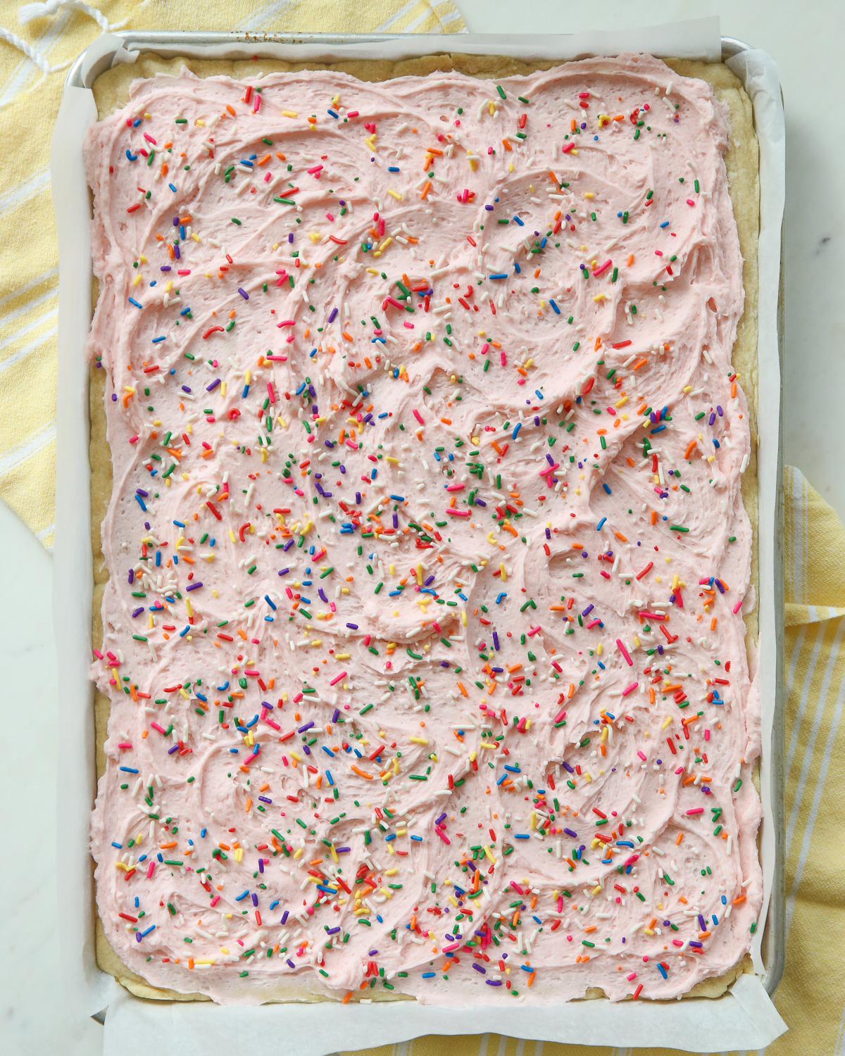 Large sheet pan filled with pink frosting and sprinkles