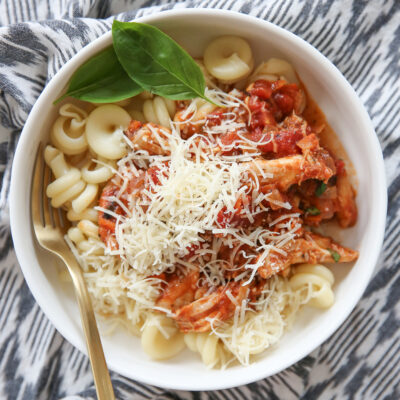 italian chicken with red sauce over pasta in a white bowl.