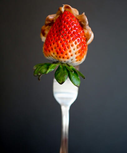 A strawberry stuffed with hazelnut cream held up by a fork. 