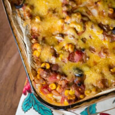 A pan full of burrito pie. Corn, tomatoes, beans, and tortillas can be seen poking through a layer of melted cheese.