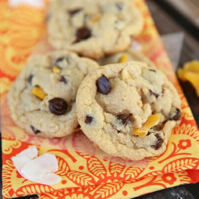 Three dark chocolate chip coconut mango cookies on an orange napkin.