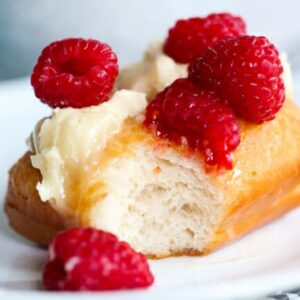 A fried scone, topped with honey butter and raspberries, with a bite taken out of it.
