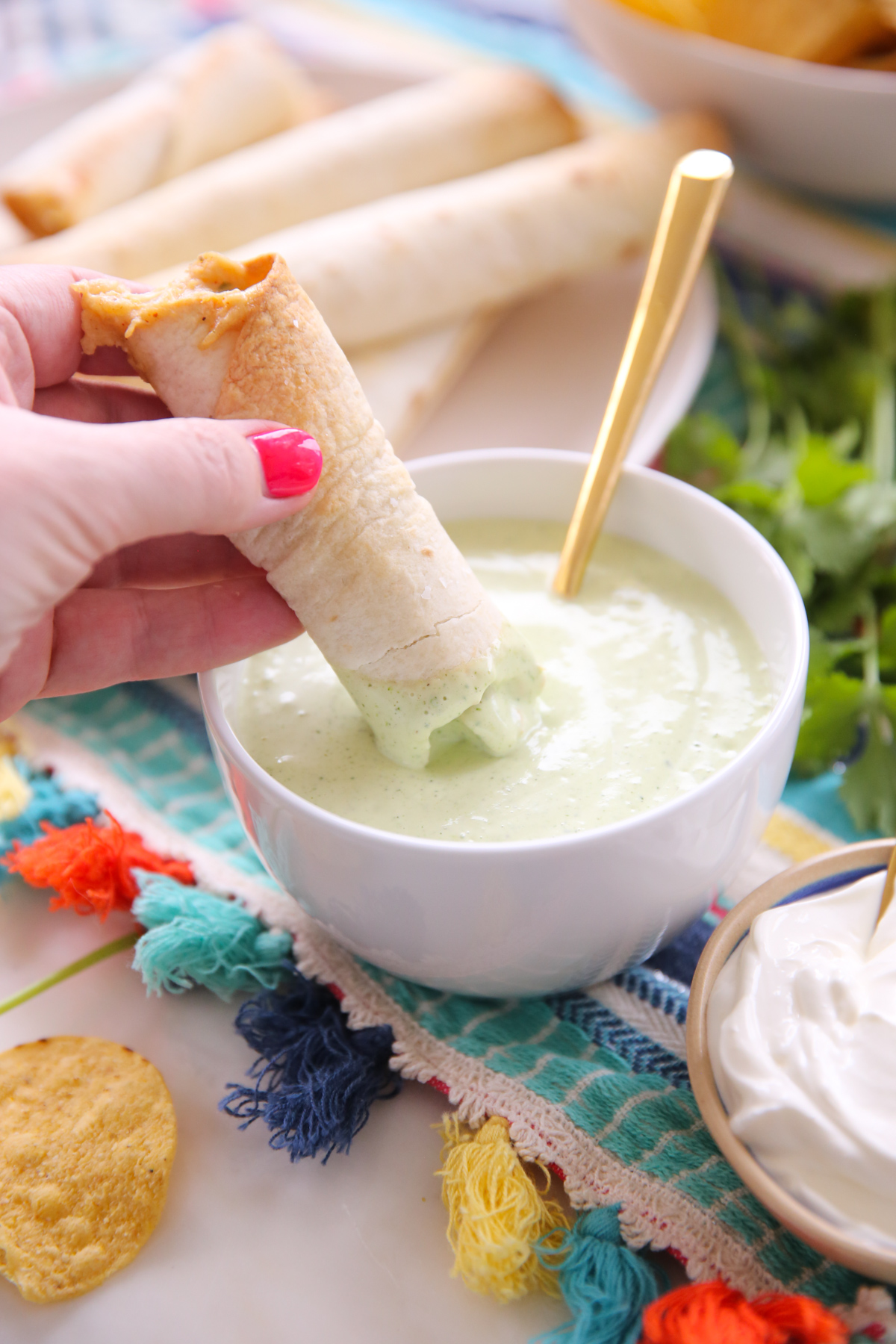 baked taquitos dipping in green sauce