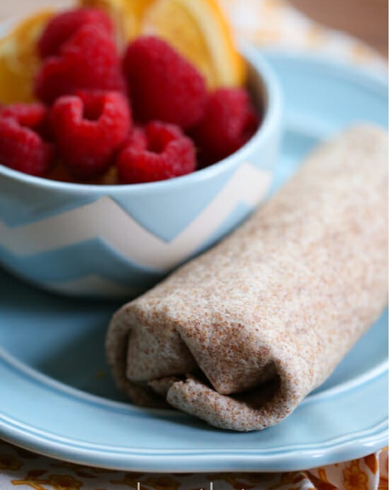 A breakfast burrito on  blue plate with a bowl of oranges and raspberries. 