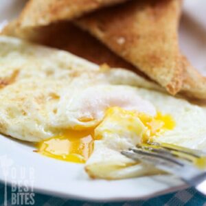 A perfect fried egg on a plate with toast.