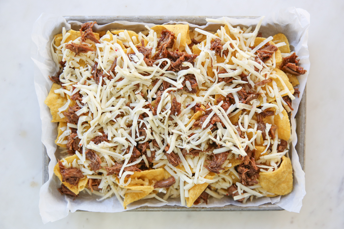 tortilla chips on a sheet pan with cheese and pork