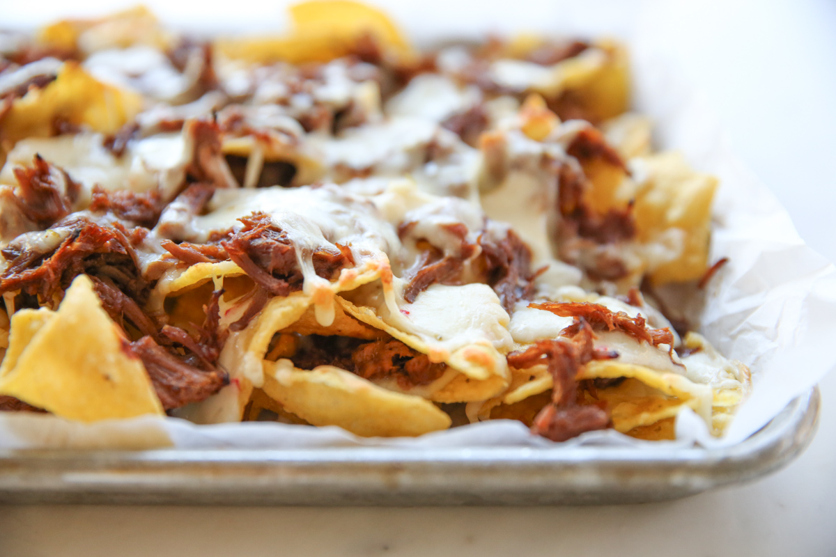 tortilla chips on a sheet pan with melted cheese and pork