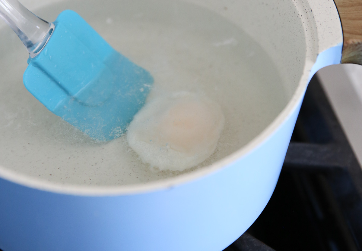 blue spatula moving a poached egg in a pot of water